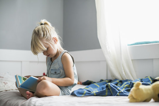 Girl sitting on bed, reading children's Bible