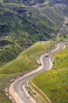 A winding road that makes it's way up and and around the Golan Heights, with remains of a train track bridge built over the Yarmouk river in the distance; Golan Heights, Israel