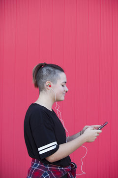 Young woman listening to music with strawberry earphones on a pink background