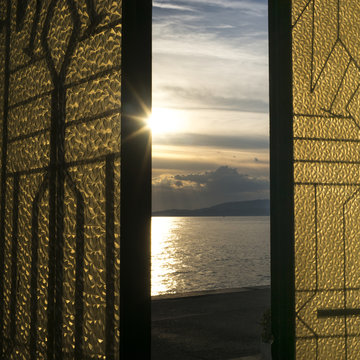 Sunlight glowing at sunset and reflected in the tranquil ocean water as viewed through a window with gold and black shutters; Panormos, Thessalia Sterea Ellada, Greece