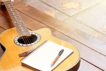 acoustic guitar with notebook and pen on wood background