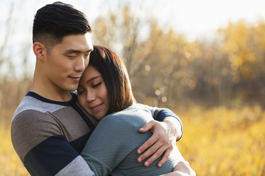 A young Asian couple enjoying quality time together outdoors in a park in autumn and embracing each other in the warmth of the sunlight during the early evening; Edmonton, Alberta, Canada