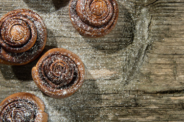 Freshly baked cinnamon buns with spices and cocoa filling on old wood table.