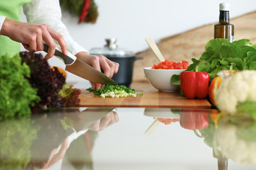 Closeup of human hands cooking vegetables salad in kitchen on the glassr table with reflection. Healthy meal and vegetarian concept