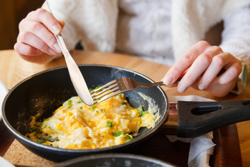 Hot omelette with greens on a pan, female hand with a fork and knife has a lunch