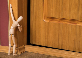 Curiosity overcomes fear. Wooden lay figure  looks at the slightly opened door.