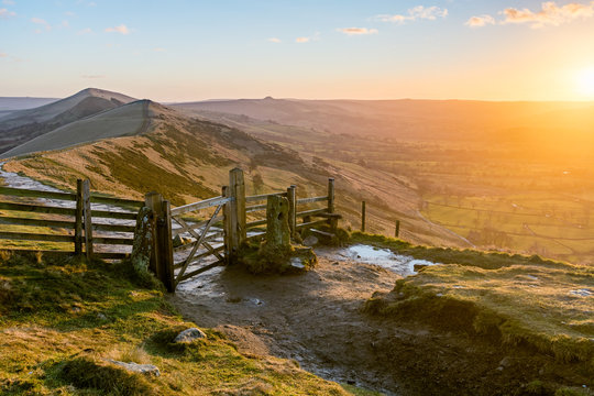 Wooden gate on bridleway at Mam Tor in the Peak District taken as the sun rises above the horizon casting golden light on landscape.