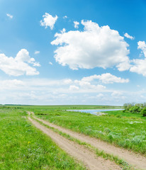 Fototapeta na wymiar green meadow with road and blue sky with clouds over them