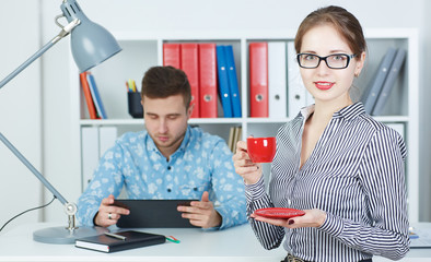 Beautiful business woman holding cup of coffee with young male business partner at the background. 