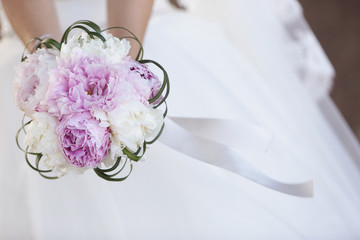 Sposa tiene in mano bouquet da matrimonio e sullo sfondo si vede l'abito da sposa