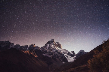 Naklejka premium Fantastic starry sky. Autumn landscape and snow-capped peaks