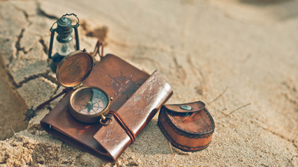 Fototapeta na wymiar Retro compass, sand glass, hourglass and brown leather notebook and pocket on sand beach in vintage style picture.