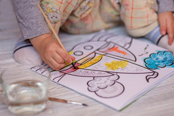 Small child draws water coloring with brush at home