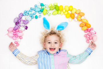 Child on Easter egg hunt. Pastel rainbow eggs.