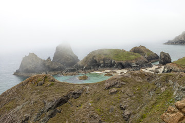 Sandy beach with turquoise sea waters hidden in rocky shore on a summer foggy day, Cornwall, Lizard, Peninsula, south west England