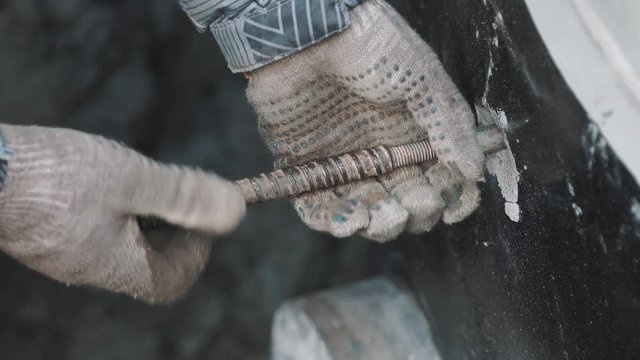 Close up man in work gloves and striped jacket untwist piece of metal rod from metal pipe in concrete