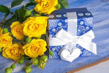 Blue present box and yellow roses on wooden tray