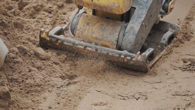 Slowmotion close up working gazoline yellow plate compactor thickening sand surface