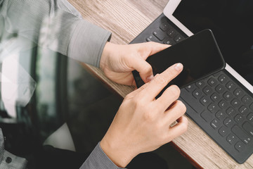 top view of businessman hand using smart phone,mobile payments online shopping,omni channel,digital tablet docking keyboard computer in modern office on wooden desk