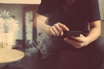 designer man hand using smart phon for mobile payments online shopping,omni channel,sitting on sofa in living room,vase rattan with plant and wooden tray on table,filter