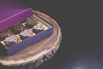 Heart shaped dark, milk, and  white chocolates in a pink, gold, and purple box, on a wooden platter