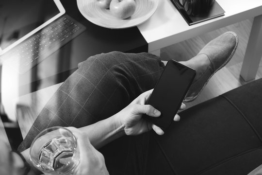 hipster hand using smart phone for mobile payments online business,glass of water,sitting on sofa in living room,green apples in wooden tray,black and white