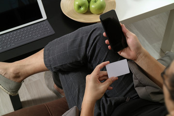hipster hand using smart phone and laptop compter,holding cradit card payments online business,sitting on sofa in living room,green apples in wooden tray