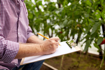 senior man writing to clipboard at farm greenhouse