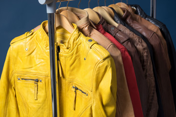 Different color leather jacket hanging on rack on blue background