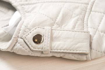Metal clasp button on white leather jacket.  Leather jacket shoulder detail. White background. Macro detail