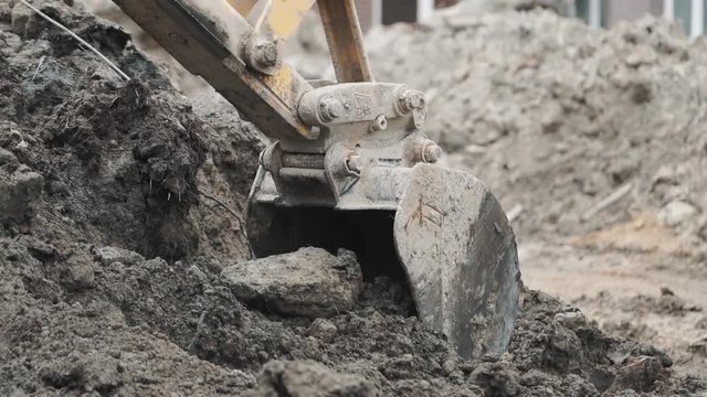 Excavator laddle digging soil sand and dirt pile at building site. Slowmotion, close up
