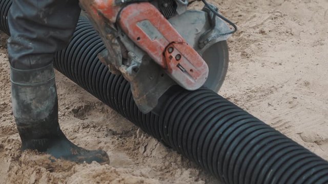 Warker nagging black ribbed plastic pipe with circular saw on sand surface, slowmotion