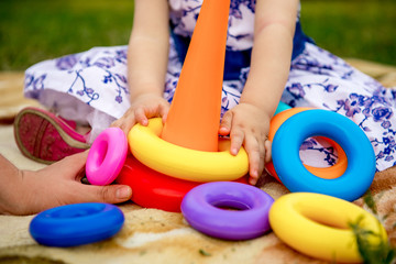 Little girl collects pyramid in the park on a blanket