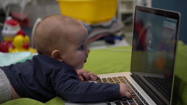 Caucasian baby lies in fron of notebook and presses keys with small fingers