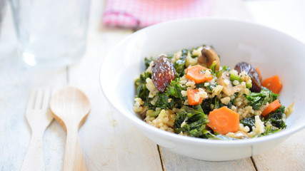 Brown rice salad with some vegetables, nuts and seeds. Meal served on a white wooden table in a rural restaurant. Empty copy space for Editor's content.