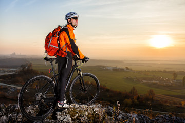View of cyclist standing with mountain bike on hill trail at sunset
