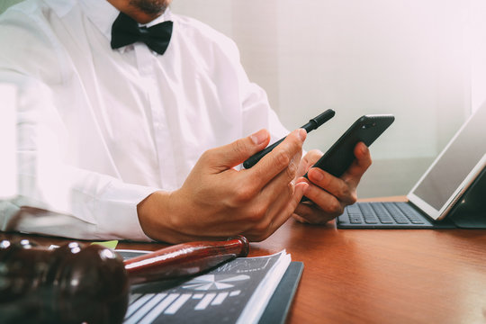 Justice and Law context.Male lawyer hand working with smart phone,digital tablet computer docking keyboard with gavel and document on wood table,filter effect