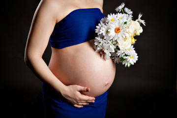 belly of a pregnant woman in a blue dress with a bouquet of daisies