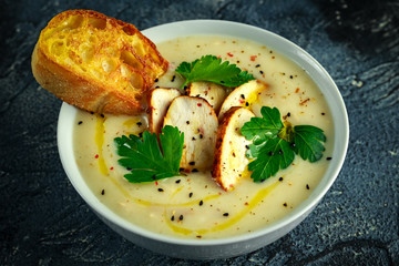 Creamy chicken soup with vegetables in bowl with chiabatta toast, parsley and nigela seeds sprinkle on stone table