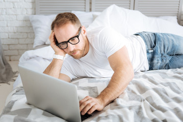 Pleasant bearded man using laptop at home