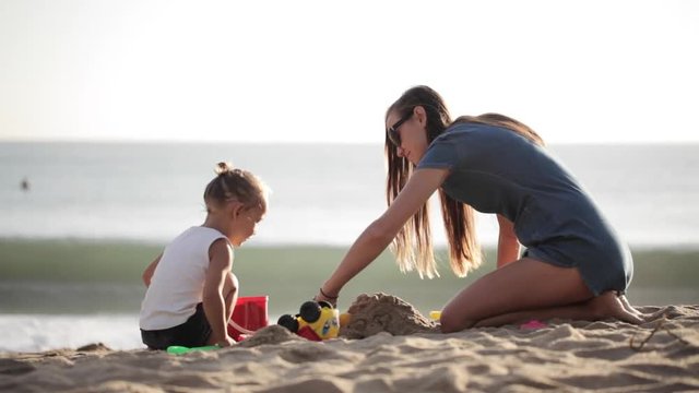 Young mother with little doughter playing with sand on the beach