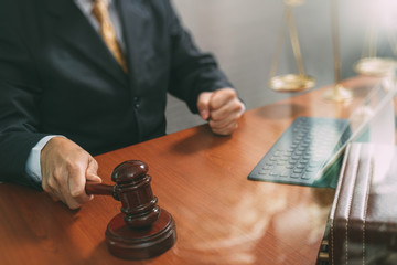 justice and law concept.Male judge in a courtroom with the gavel,working with smart phone,digital tablet computer docking keyboard,brass scale,on wood table