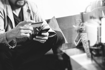 hipster hand using smart phone,digital tablet docking keyboard,holding cradit card payments online business,sitting on sofa in living room,work at home concept,black and white