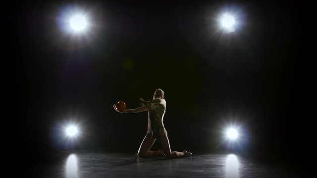 Gymnast with the ball in his hands doing acrobatic moves. Black background. Light rear