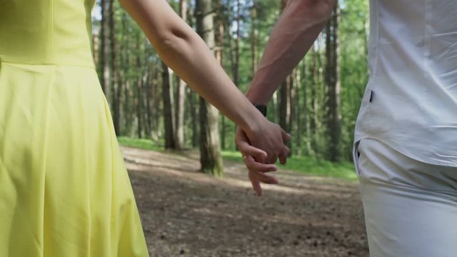 Young lovely couple walking in forest and join hands