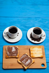 Two cups of coffee and toast with chocolate on a blue wooden table