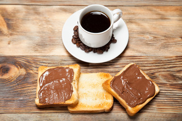 cup with coffee, toast and chocolate on wooden table