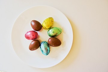 Colourful chocolate Easter eggs on the white plate on the white table