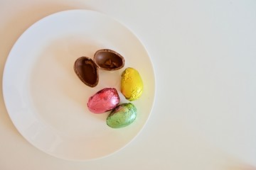 Colourful chocolate Easter eggs on the white plate on the white table