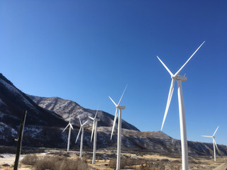 Environmentally friendly wind turbines with massive blades turn in the wind producing green, renewable energy.  Blue skies. Mountains and grass. Spanish Fork Canyon, Spanish Fork, Utah, United States.